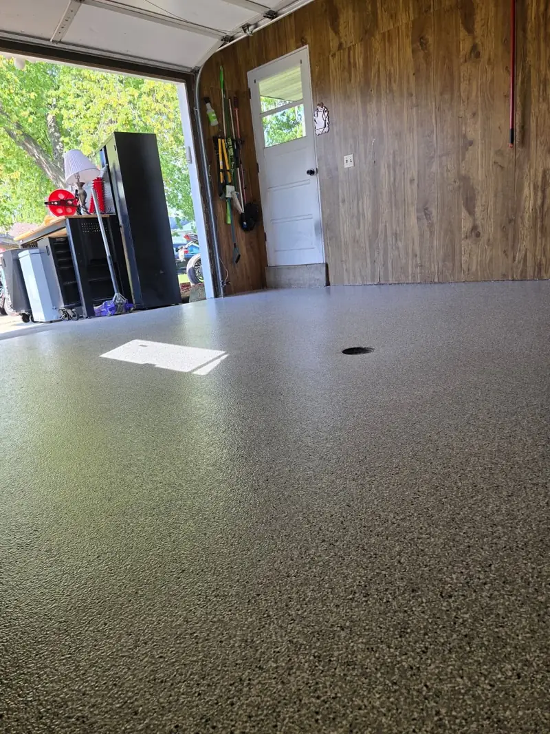 Low-angle view of a finished gray flake garage floor and drain with door open, Allouez, WI