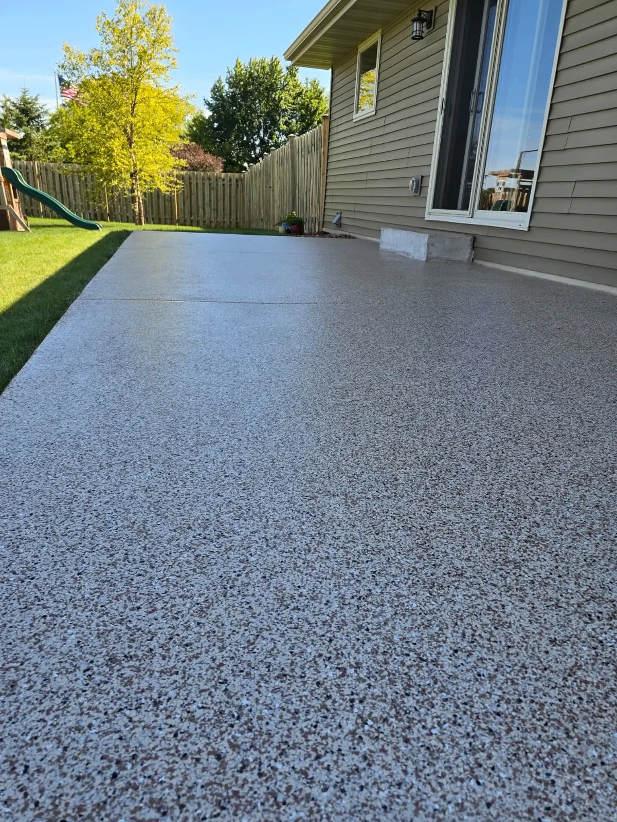 Flake-coated concrete patio next to home with backyard view