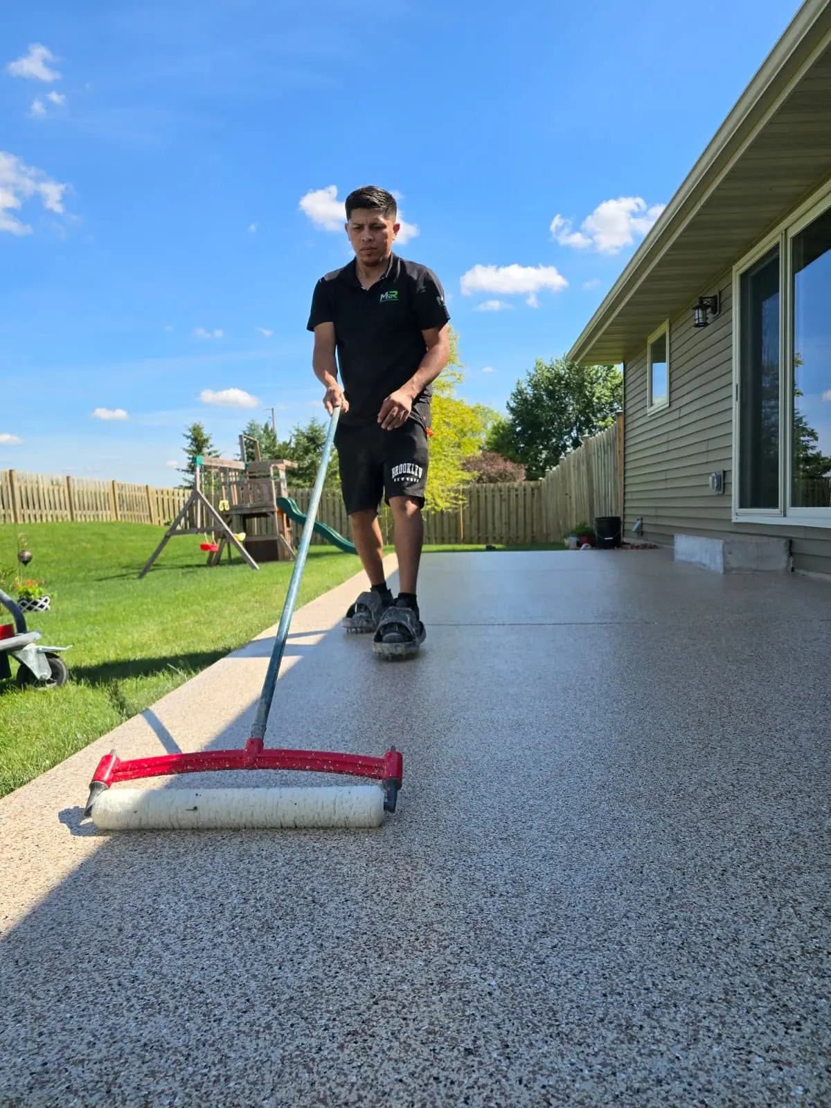 Technician applying top coat to flake patio with roller